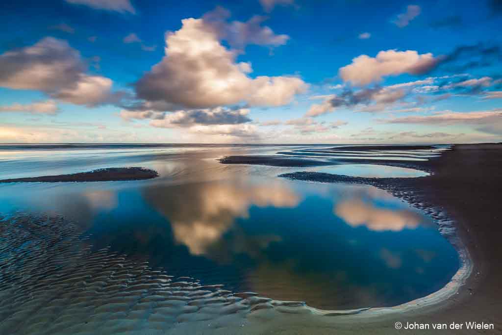 reflecties van wolken in het natte zand