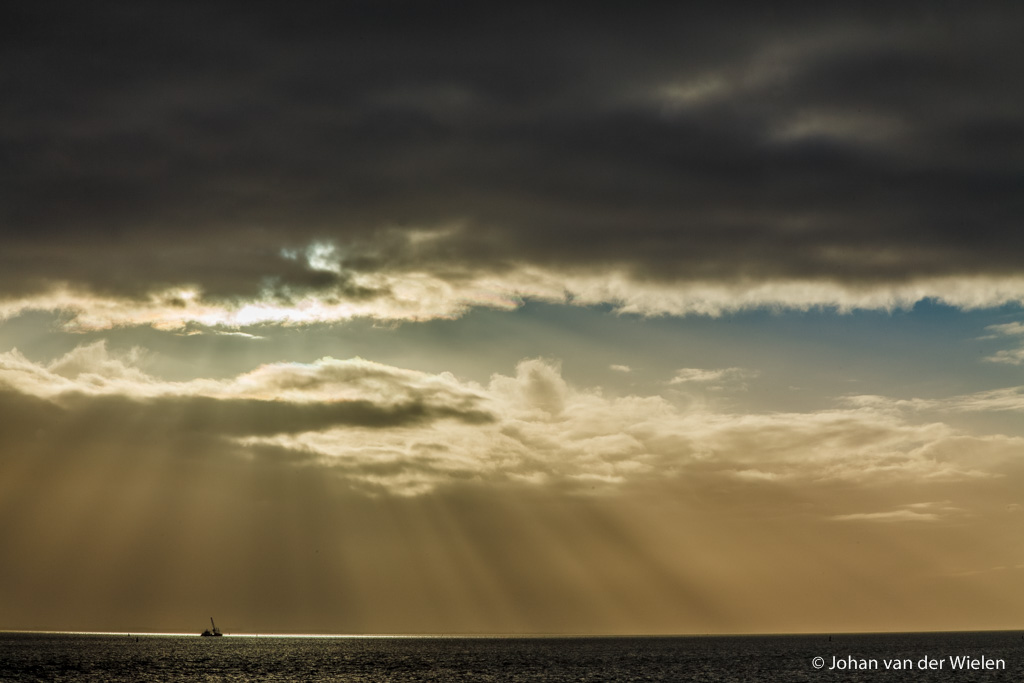 de zon priemt door een gat in het donkere wolkendek en verlicht precies een baggerschip in de waddenzee