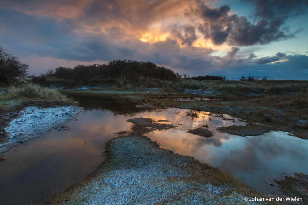 de opkomende zon verlicht de wolken met warme kleuren, reflectie van de wolken in de poelen van de kwelders