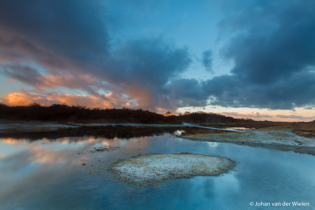 de opkomende zon verlicht de wolken met warme kleuren, reflectie van de wolken in de poelen van de kwelders
