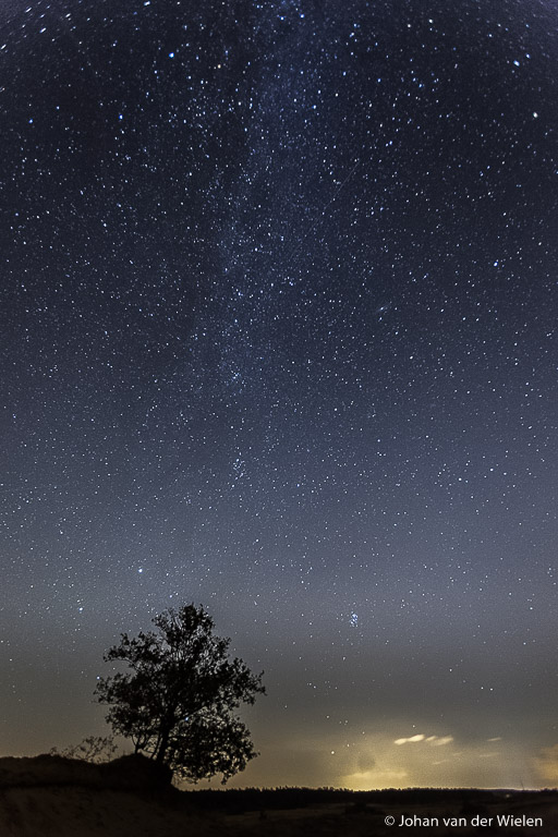 De melkweg is moeilijk te zien, maar hier zichtbaar vanaf het Kootwijkerzand met in de verte lichtvervuiling van de stad Apeldoorn.