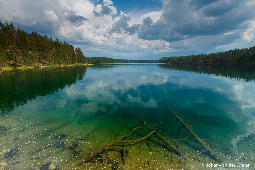 wolkenlucht reflecteert in het heldere meer, op de bodem liggen boomstammen; cloudy sky reflecting in the clear lake, at the bottom are trunks
